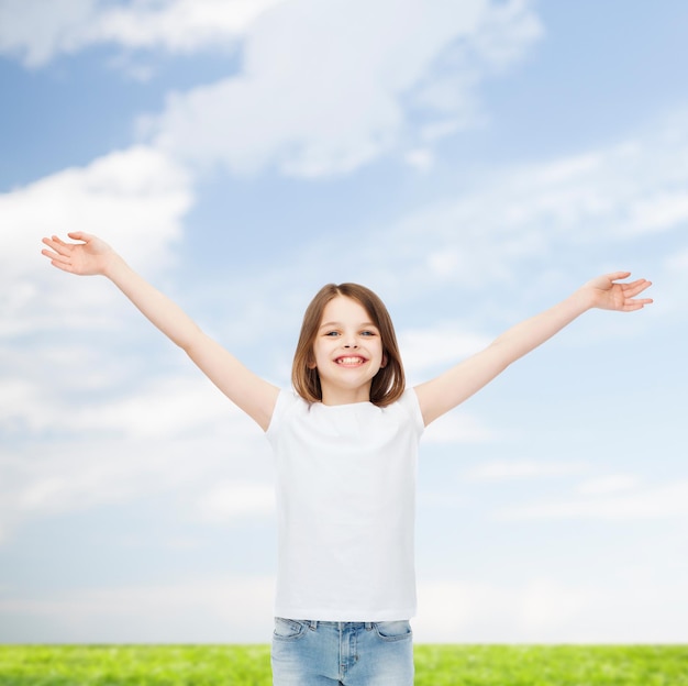 concept de publicité, d'enfance, de geste et de personnes - petite fille souriante en t-shirt blanc avec bras tendus sur fond naturel