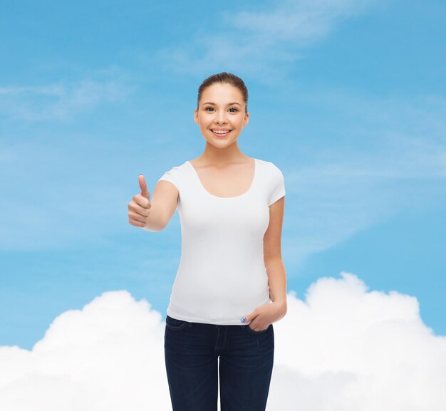 concept de publicité, de rêve, de geste et de personnes - jeune femme souriante en t-shirt blanc vierge montrant les pouces vers le haut sur fond de ciel bleu