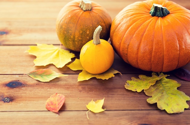 concept de récolte, de saison, de publicité et d'automne - gros plan de citrouilles et de feuilles sur une table en bois à la maison