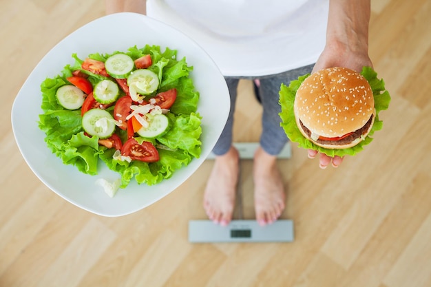 Concept de régime, femme choisissant entre junk burger et salade fraîche.