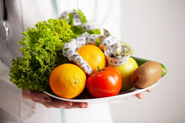 Concept de régime, nutritionniste tenant une assiette pleine de fruits frais avec un ruban à mesurer