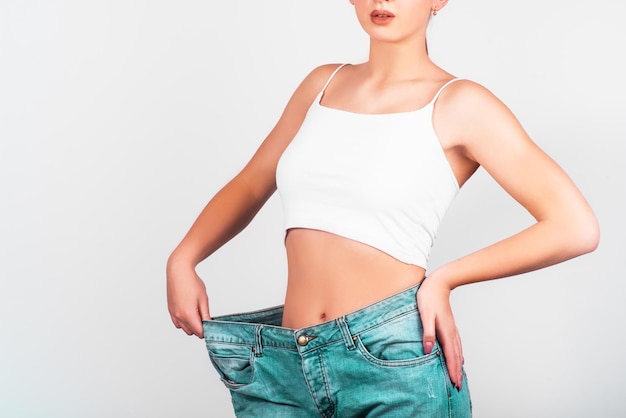 Concept de régime et perte de poids Femme en jeans surdimensionnés sur fond blanc Soins du corps
