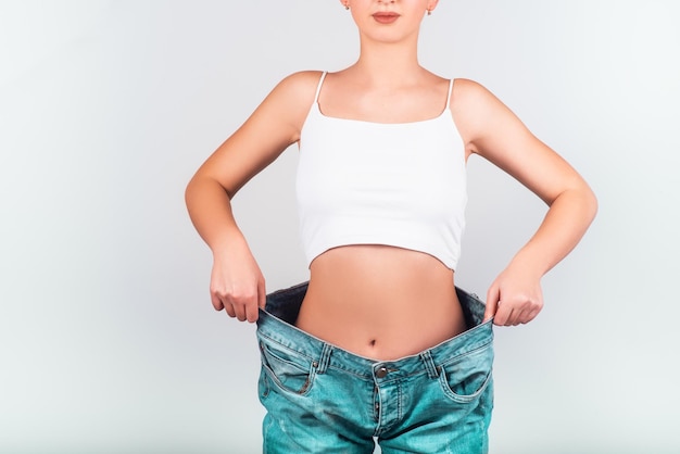Concept de régime et perte de poids Femme en jeans surdimensionnés sur fond blanc Soins du corps