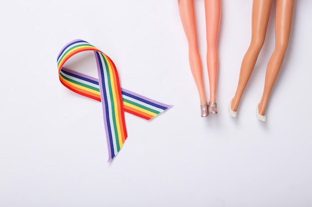 Concept de relation lesbienne de la communauté lgbt Pieds de poupées et ruban de symbole lgbt arc-en-ciel sur fond blanc