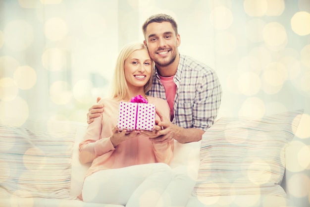 concept de relations, d'amour, de personnes, d'anniversaire et de vacances - homme heureux donnant une boîte cadeau à une femme à la maison sur fond de lumières