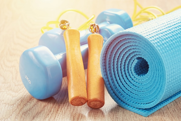 Concept de remise en forme avec des haltères bleus, un tapis de yoga et une corde à sauter