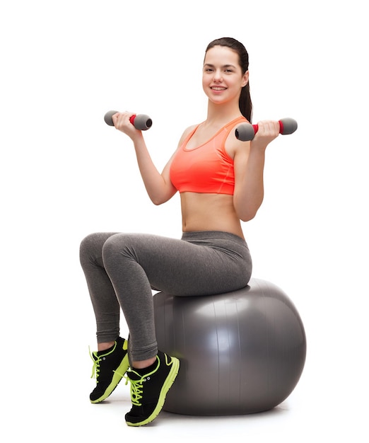 concept de remise en forme et de régime - adolescente souriante avec des haltères assis sur un ballon de fitness