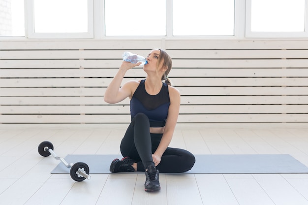 Concept de remise en forme, de santé et de sport - jeune femme assise les jambes croisées et buvant de l'eau de la bouteille après l'entraînement.