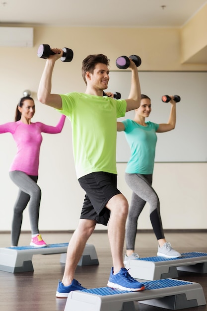 concept de remise en forme, de sport, d'aérobic et de personnes - groupe de personnes souriantes travaillant avec des haltères fléchissant les muscles sur des plates-formes de marche dans la salle de sport