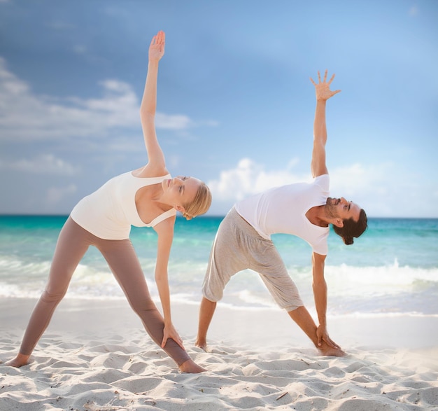 concept de remise en forme, de sport, d'amitié et de style de vie - couple faisant des exercices de yoga sur la plage d'été