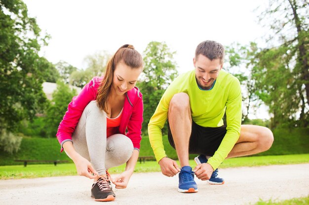 concept de remise en forme, de sport, d'amitié et de style de vie - couple souriant attachant des lacets à l'extérieur