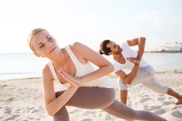 concept de remise en forme, de sport, d'amitié et de style de vie - gros plan d'un couple faisant des exercices de yoga sur la plage