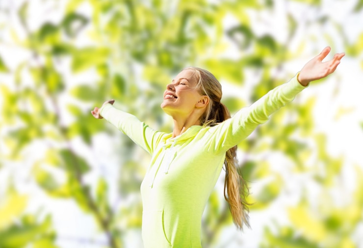 Photo concept de remise en forme, de sport, de bonheur et de personnes - femme heureuse levant les mains sur fond de feuilles d'arbre vert