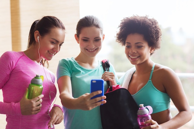 concept de remise en forme, de sport, d'entraînement, de gym et de style de vie - groupe de femmes heureuses avec des bouteilles et un smartphone dans la salle de gym