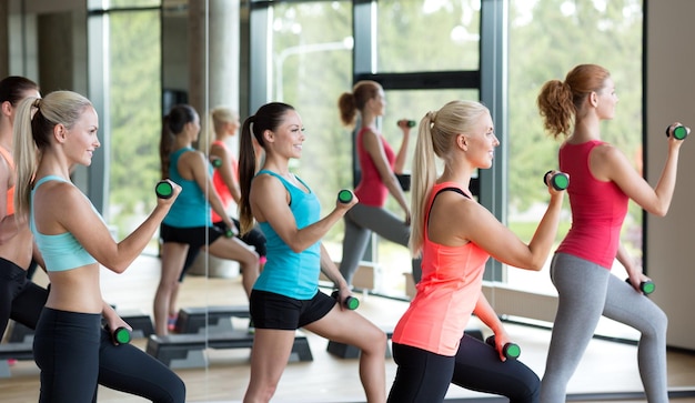 concept de remise en forme, de sport, d'entraînement, de gym et de style de vie - groupe de femmes travaillant avec des haltères et des steppers dans la salle de gym