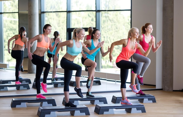 concept de remise en forme, de sport, d'entraînement, de gym et de style de vie - groupe de femmes travaillant avec des steppers dans la salle de gym