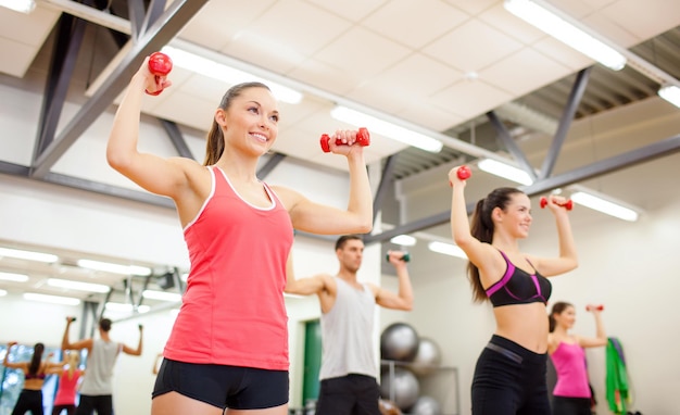 concept de remise en forme, de sport, d'entraînement, de gym et de style de vie - groupe de personnes souriantes travaillant avec des haltères dans la salle de gym