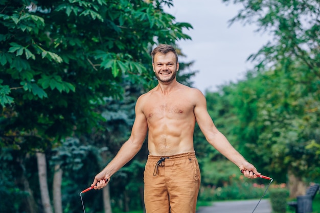 Concept de remise en forme, sport, entraînement et mode de vie - athlète en bonne santé saut torse nu avec corde à sauter en plein air.