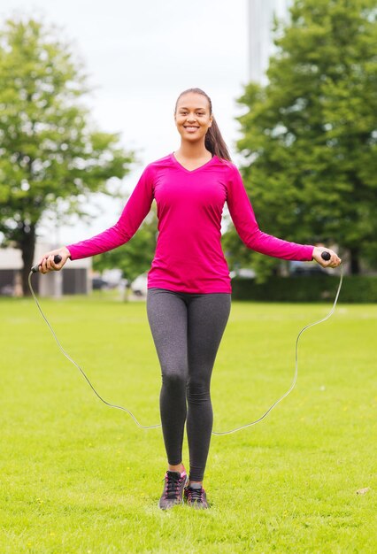 concept de remise en forme, de sport, d'entraînement, de parc et de style de vie - femme afro-américaine souriante faisant de l'exercice avec une corde à sauter à l'extérieur