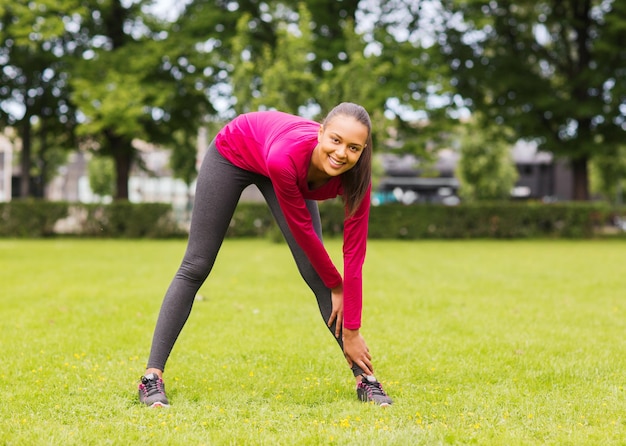 concept de remise en forme, de sport, d'entraînement, de parc et de style de vie - femme souriante qui s'étend de la jambe à l'extérieur