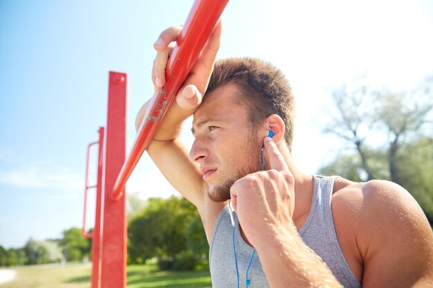 concept de remise en forme, de sport, d'entraînement et de style de vie - jeune homme avec des écouteurs écoutant de la musique et faisant de l'exercice sur une barre horizontale à l'extérieur