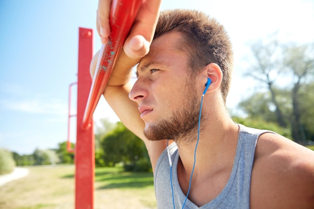 concept de remise en forme, de sport, d'entraînement et de style de vie - jeune homme avec des écouteurs écoutant de la musique et faisant de l'exercice sur une barre horizontale à l'extérieur