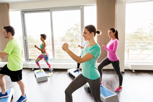 concept de remise en forme, de sport, d'exercice, d'aérobic et de personnes - groupe de personnes souriantes travaillant sur des plates-formes de marche dans la salle de sport