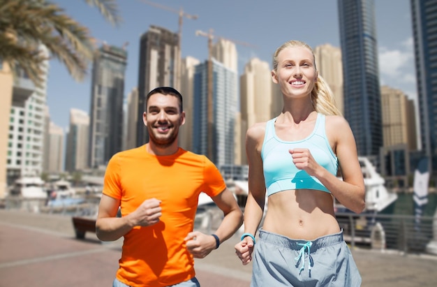 concept de remise en forme, de sport, d'exercice et de mode de vie sain - couple souriant courant ou faisant du jogging sur fond de rue de la ville de dubaï