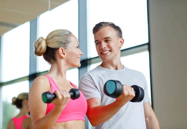 concept de remise en forme, de sport, d'exercice et de régime - jeune femme souriante et entraîneur personnel avec des haltères dans la salle de gym