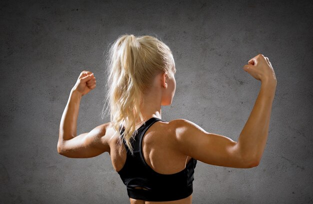concept de remise en forme, de sport et de force - une femme sportive se forme en arrière en fléchissant ses biceps sur fond de mur en béton