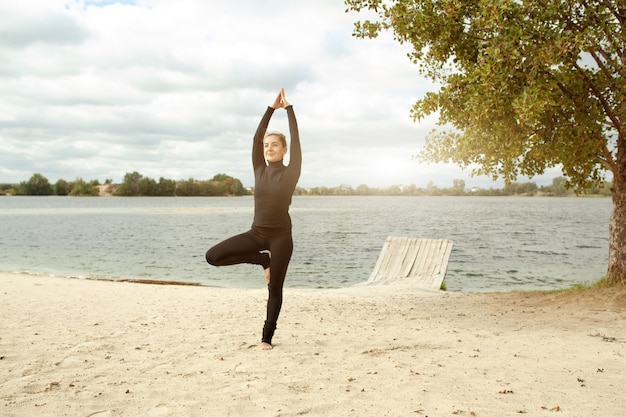 Concept de remise en forme, sport, gens et style de vie - jeune femme faisant des exercices de yoga sur la plage
