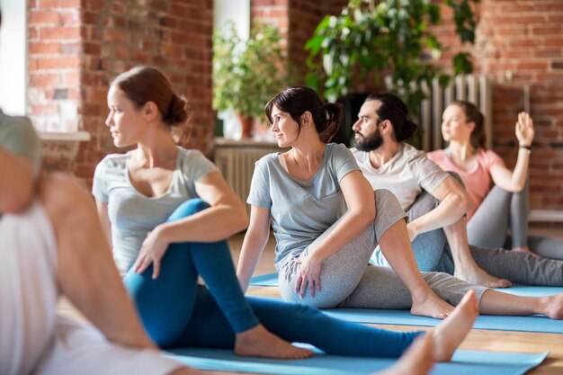 concept de remise en forme, de sport et de mode de vie sain - groupe de personnes faisant du yoga assis dans une pose de torsion de la colonne vertébrale dans une salle de sport ou un studio