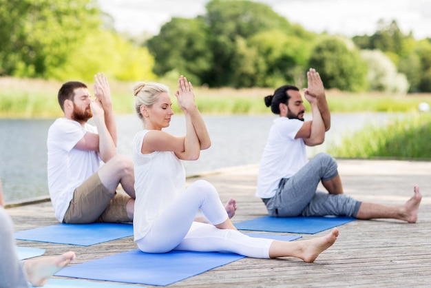 concept de remise en forme, de sport et de mode de vie sain - groupe de personnes faisant de l'exercice de yoga et méditant à l'extérieur sur la couchette de la rivière ou du lac