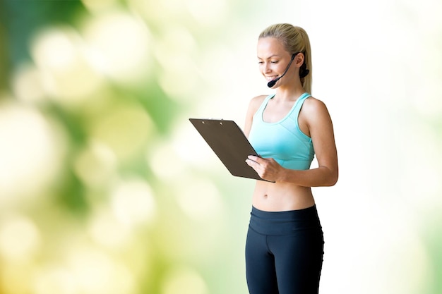 concept de remise en forme, de sport et de personnes - entraîneur sportif de femme heureuse avec microphone et presse-papiers sur fond naturel vert