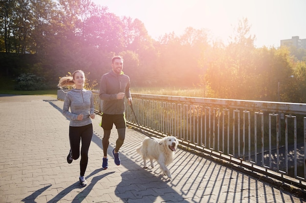 concept de remise en forme, de sport, de personnes et de jogging - couple heureux avec un chien qui court à l'extérieur