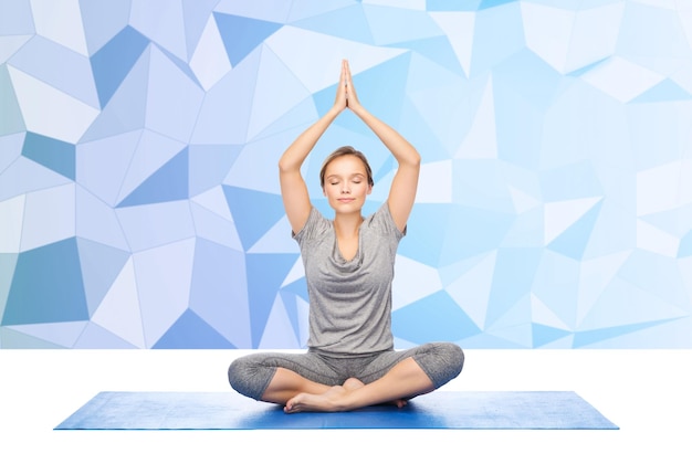 Photo concept de remise en forme, de sport, de personnes et de mode de vie sain - femme faisant du yoga méditation en pose de lotus sur tapis sur fond low poly
