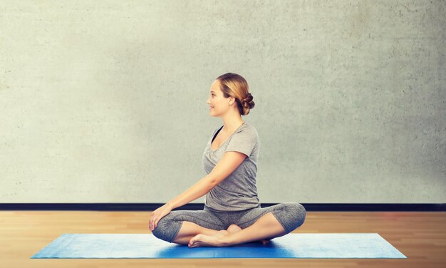 Photo concept de remise en forme, de sport, de personnes et de mode de vie sain - femme faisant du yoga en torsion pose sur tapis sur fond de salle de gym