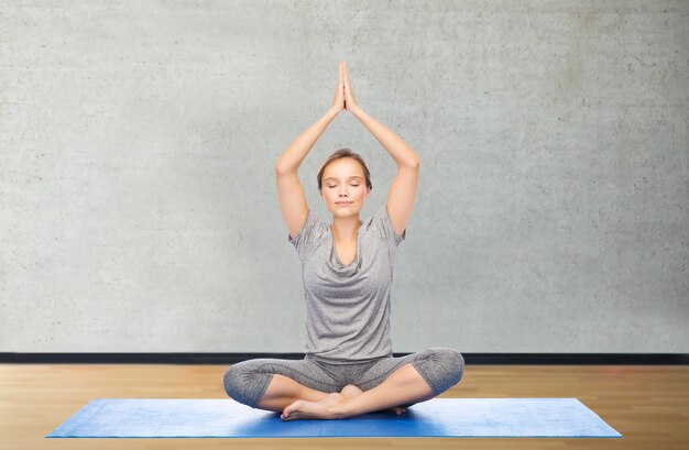 Photo concept de remise en forme, de sport, de personnes et de mode de vie sain - femme faisant de la méditation de yoga dans la pose de lotus sur un tapis sur fond de salle de gym