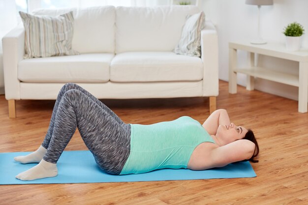 concept de remise en forme, de sport, de personnes et de mode de vie sain - jeune femme de taille plus faisant de l'exercice sur un tapis à la maison