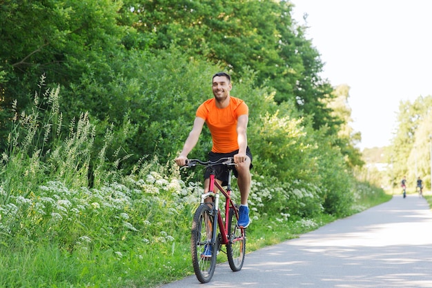 concept de remise en forme, de sport, de personnes et de mode de vie sain - jeune homme heureux faisant du vélo à l'extérieur