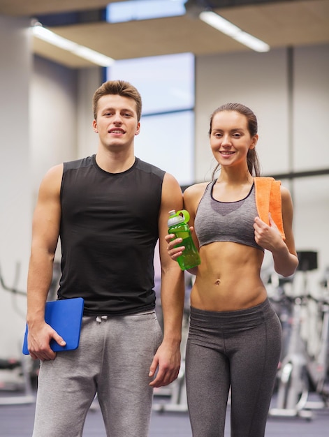 concept de remise en forme, de sport, de personnes et de style de vie - couple heureux dans une salle de sport avec eau, serviette et ordinateur tablette