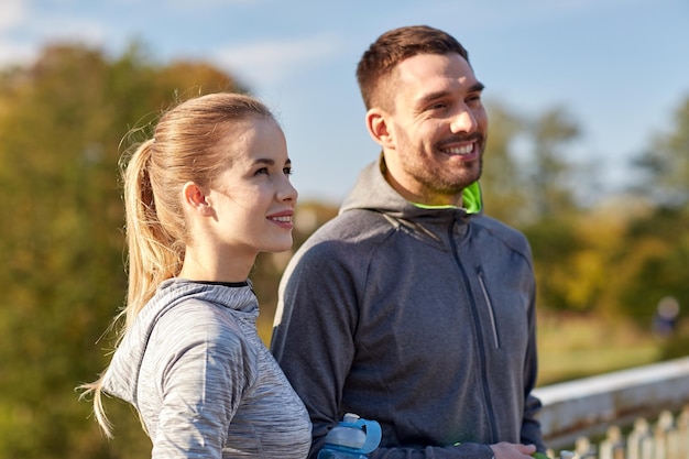 concept de remise en forme, de sport, de personnes et de style de vie - couple souriant avec des bouteilles d'eau à l'extérieur