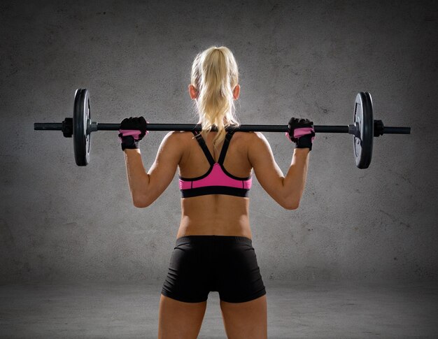 concept de remise en forme, de sport et de régime - femme sportive faisant de l'exercice avec des haltères de dos sur fond de mur en béton