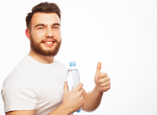 Concept de remise en forme, sport et style de vie. souriant homme sportif musclé vêtu d'une chemise blanche avec une bouteille d'eau isolé sur blanc.