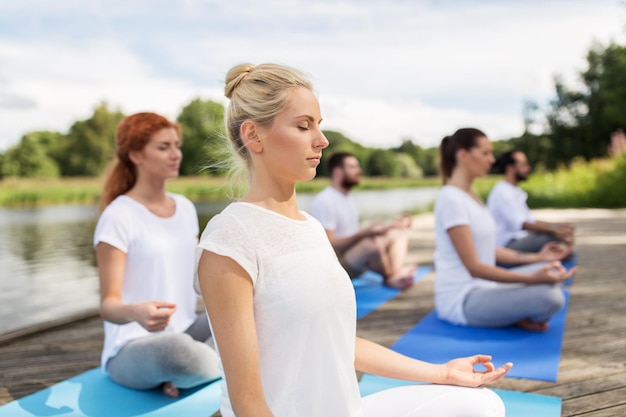 concept de remise en forme, de sport, de yoga et de mode de vie sain - groupe de personnes méditant dans la pose de lotus sur la couchette de la rivière ou du lac