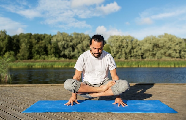 concept de remise en forme, de sport, de yoga, de personnes et de mode de vie sain - l'homme faisant de l'échelle pose une variation de lotus sur un tapis à l'extérieur sur la couchette de la rivière ou du lac