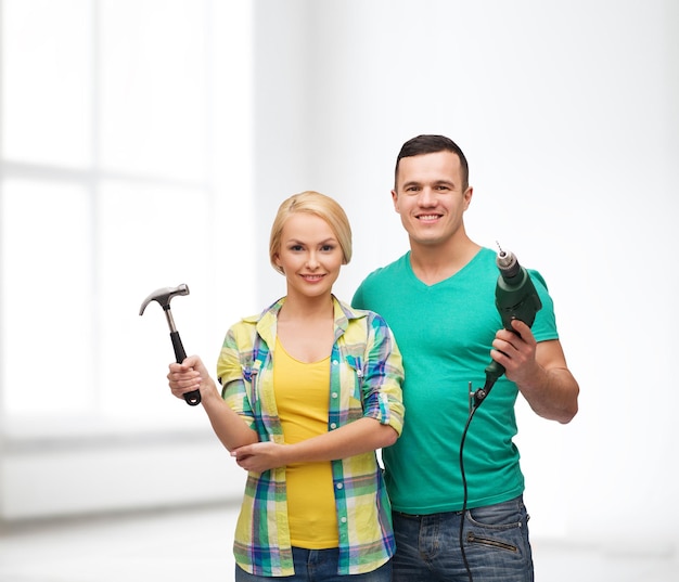 concept de réparation, de construction et d'entretien - couple souriant avec marteau et perceuse sur fond blanc