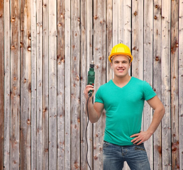 concept de réparation, de construction et d'entretien - ouvrier masculin souriant dans un casque de protection avec perceuse