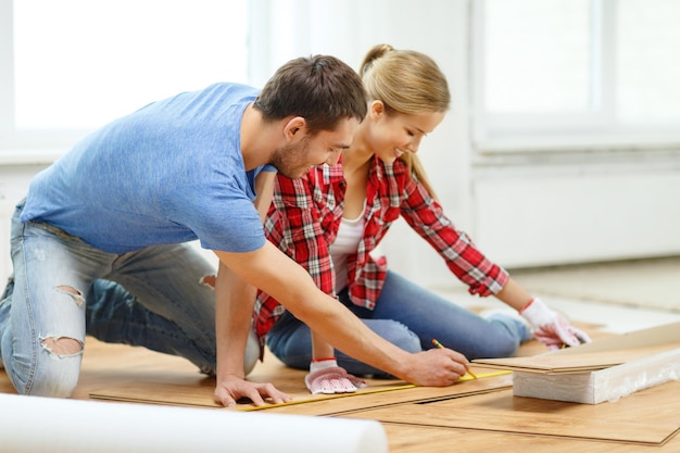 concept de réparation, de construction et de maison - couple souriant mesurant le parquet