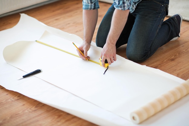 concept de réparation, de construction et de maison - gros plan de mains masculines mesurant le papier peint